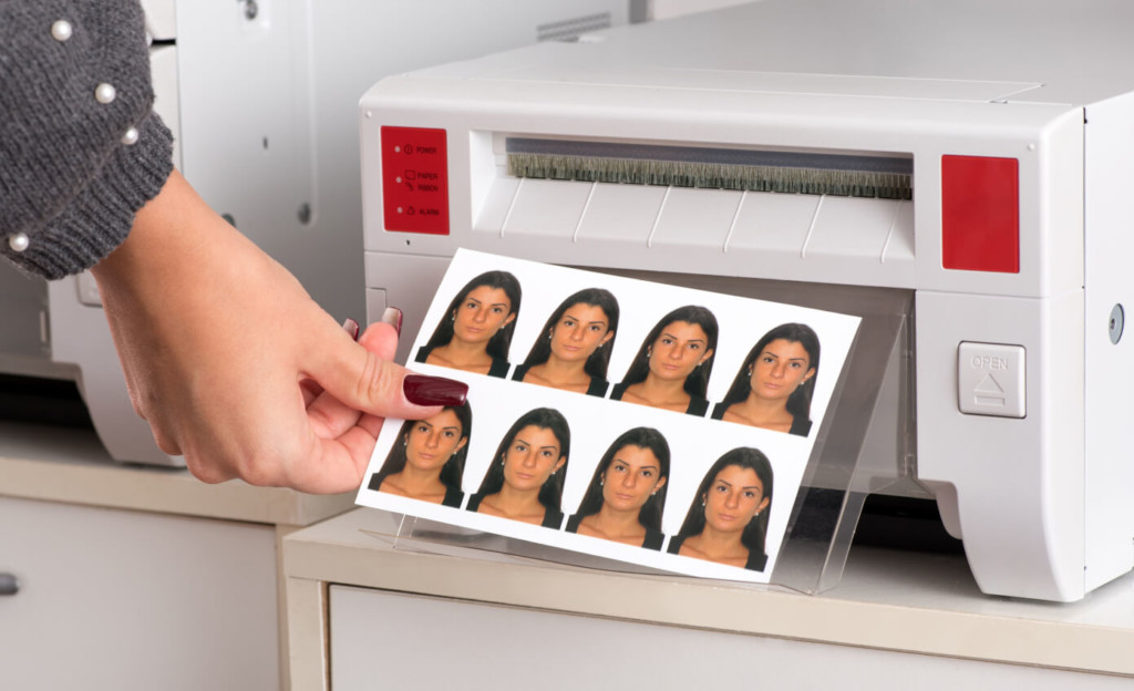 Passport Photo Print Person removing a completed passport photo print sheet from a photo printer, showing multiple identical headshots ready for official document use.