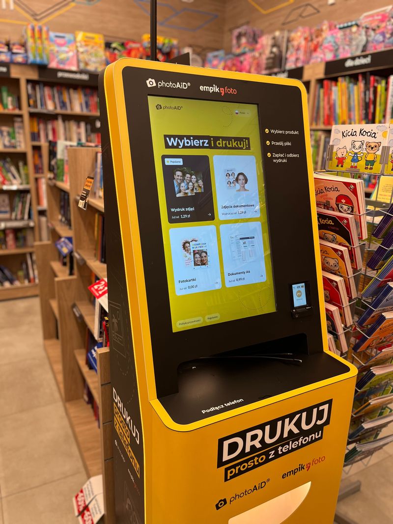 Żółto-czarny foto kiosk PhotoAiD do wydruku zdjęć i dokumentów w Empik Auchan Komorniki