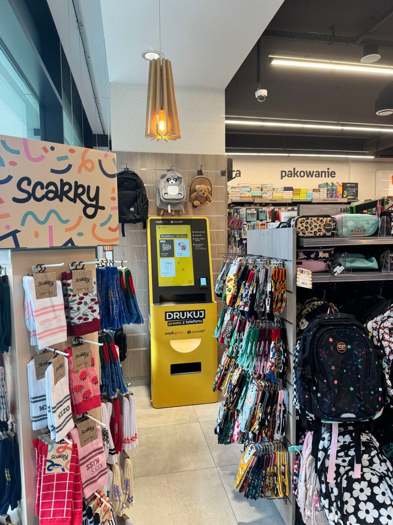 Żółto-czarny foto kiosk PhotoAiD przy dziale plecaków w Papierniku by Empik na Żoliborzu