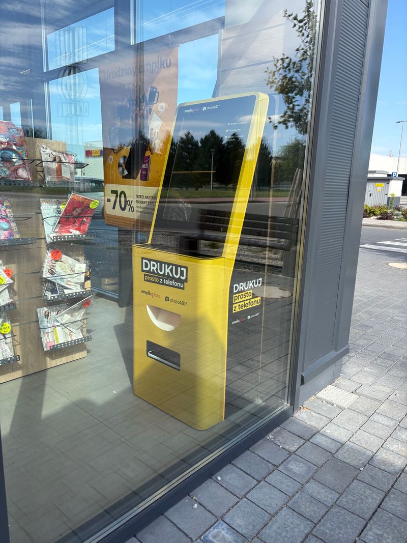 Foto kiosk PhotoAiD widoczny od strony parkingu przez witrynę salonu Empik w Prudniku