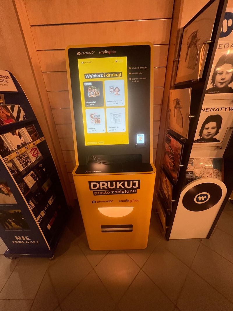 Żółto-czarny foto kiosk PhotoAiD do wydruku zdjęć i dokumentów w Empik Poznań Ratajczaka
