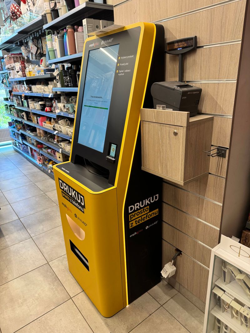 Żółto-czarny foto kiosk PhotoAiD do wywoływania zdjęć i druku dokumentów A4 w Empik Warszawa Obozowa