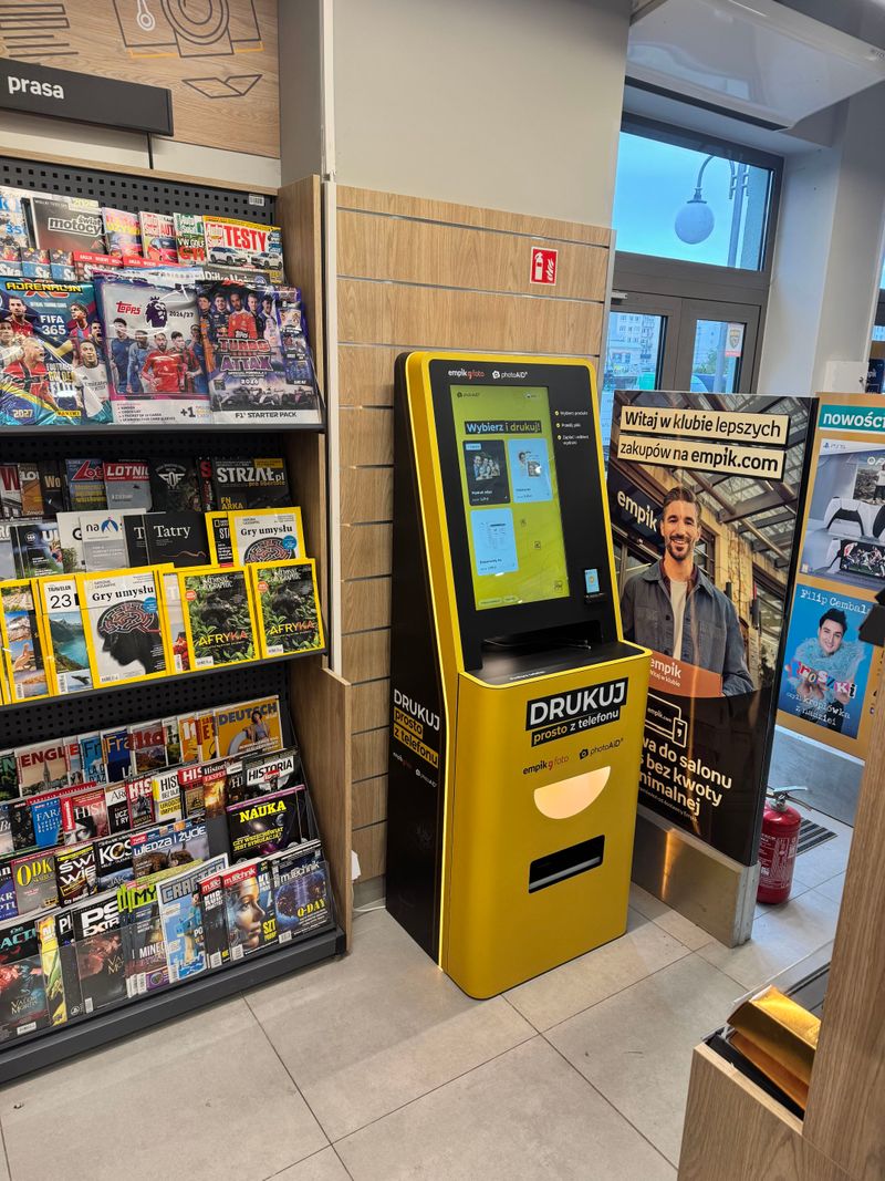 Foto kiosk PhotoAiD przy wejściu do salonu Empik Powstańców Śląskich, obok półki z prasą